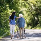 A caregiver walking outdoors alongside an older woman using a walker