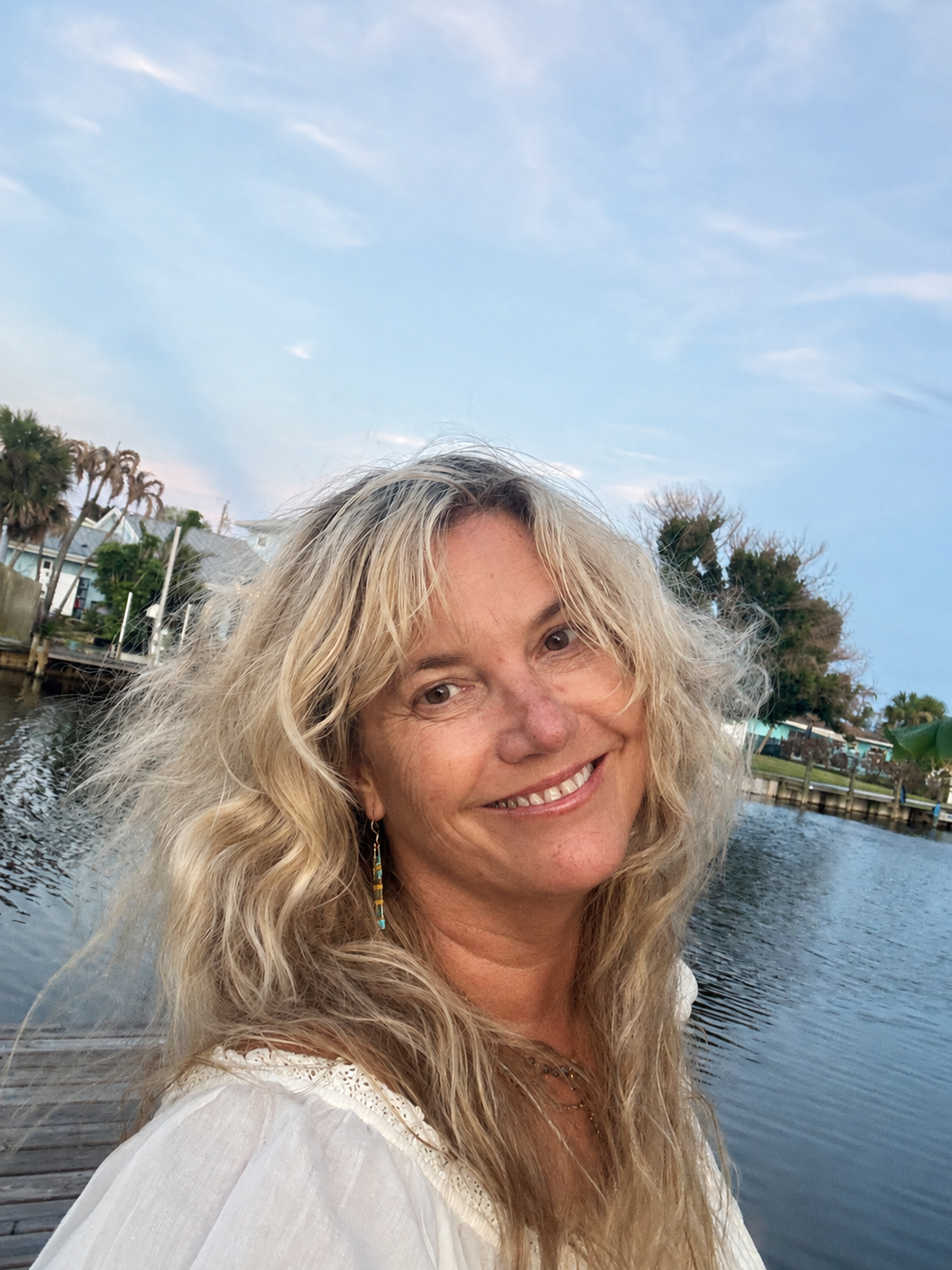 Mary Jo Landry smiling on a dock with water and palm trees behind her