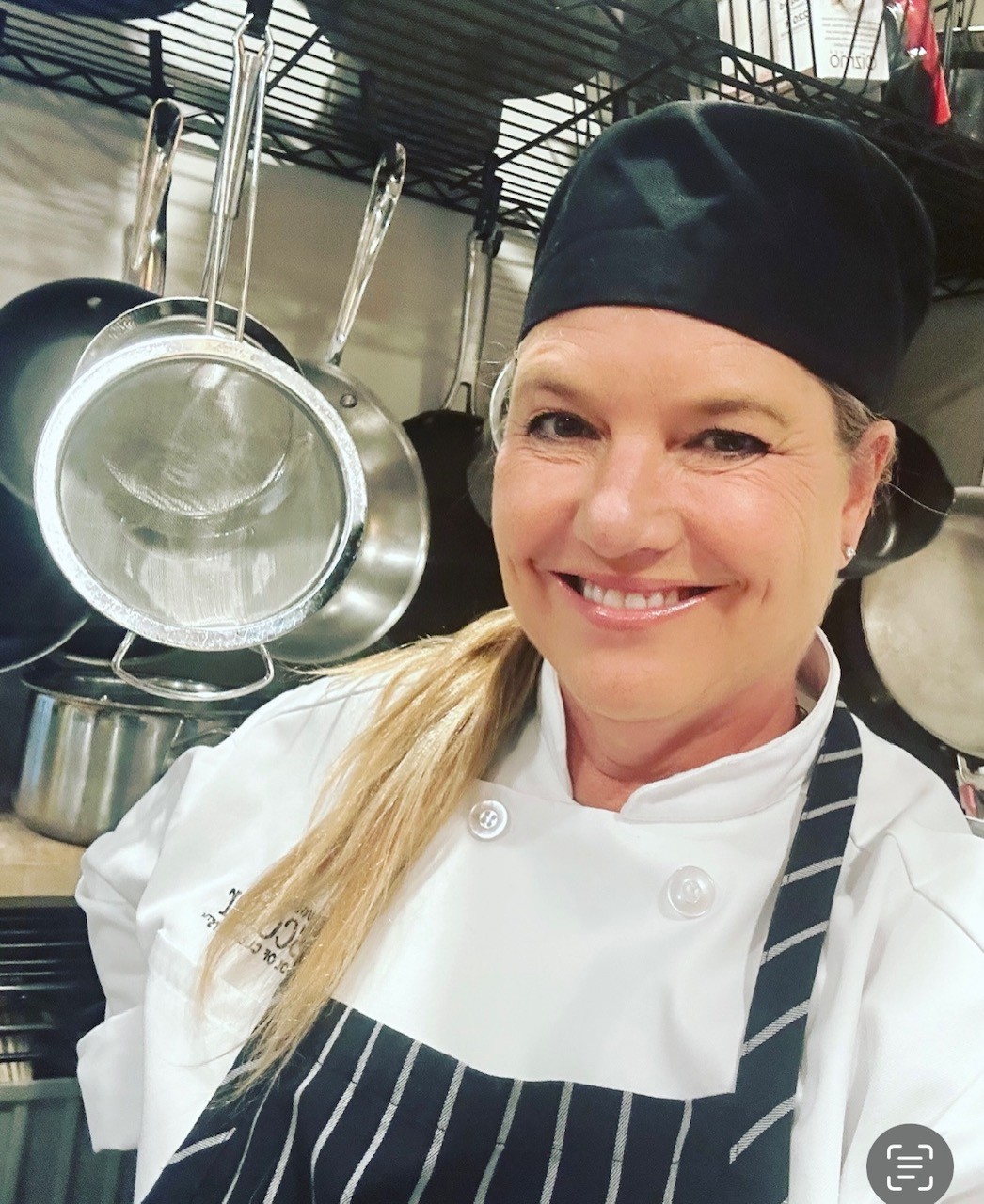 Mary Jo Landry in a white chef's coat and black skull cap in a commercial kitchen